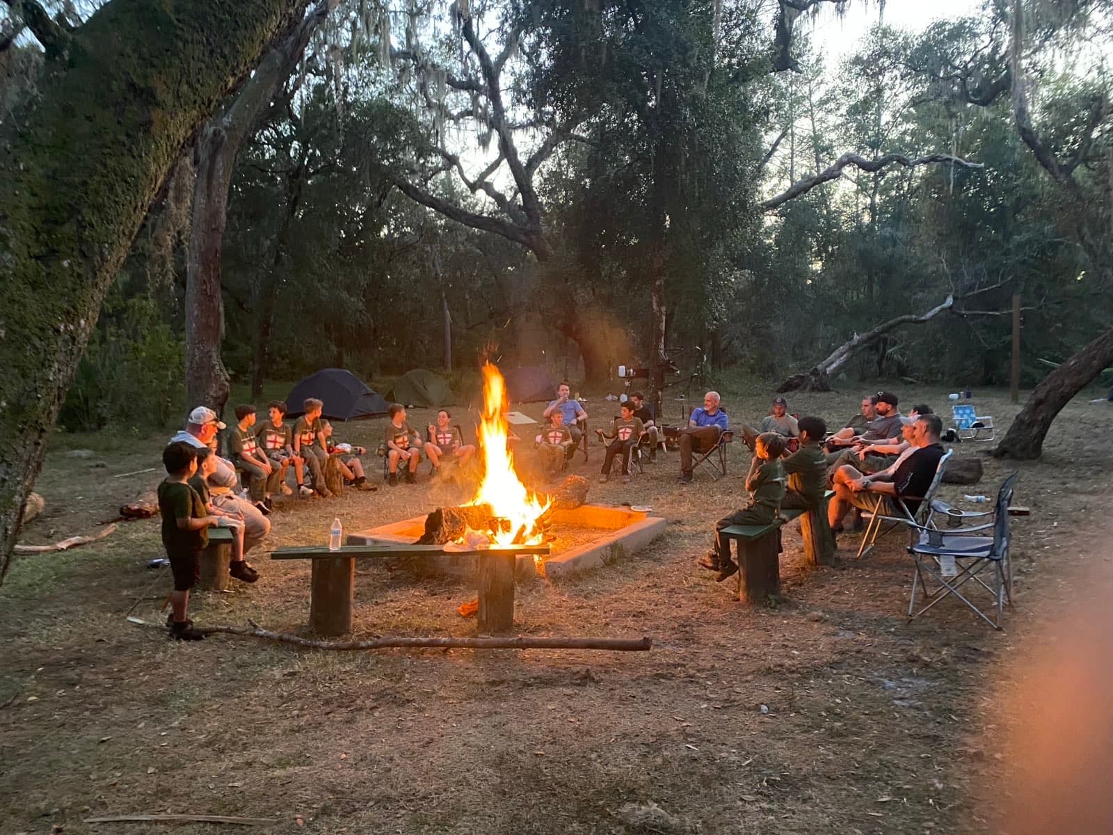 Troop 51 seated around a fire in the woods at dusk