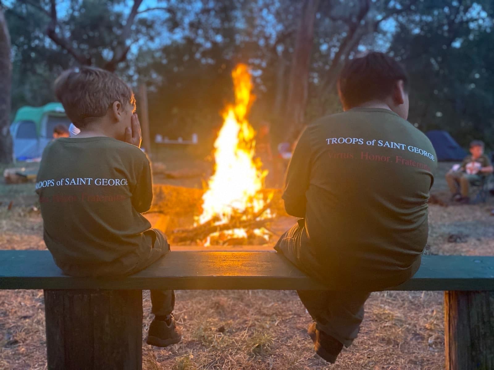 Two boys seated beside a campfire